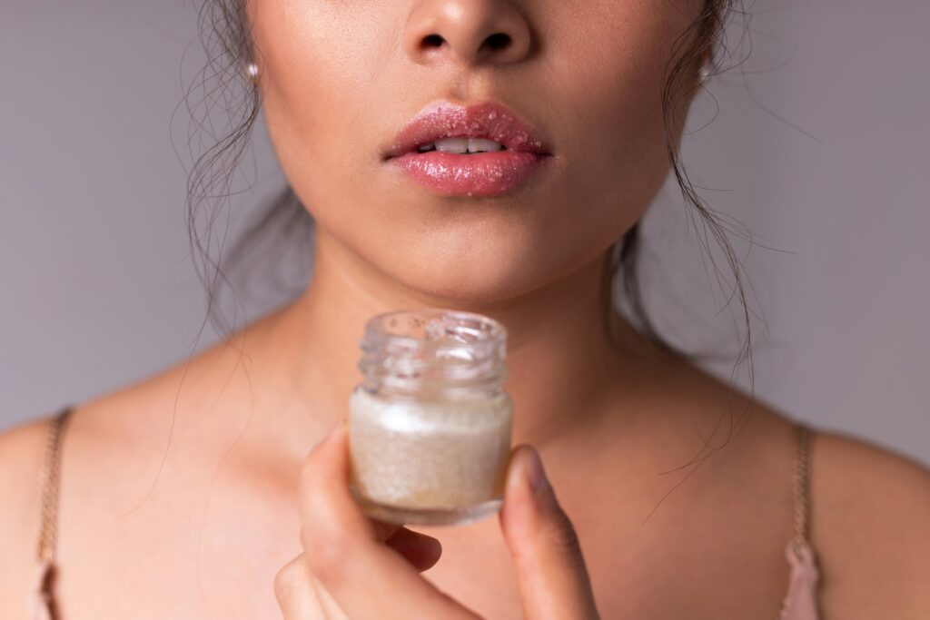 Mulher aplicando esfoliante labial caseiro com brilho, representando cuidados de beleza e tendência clean girl estética em skincare artesanal.