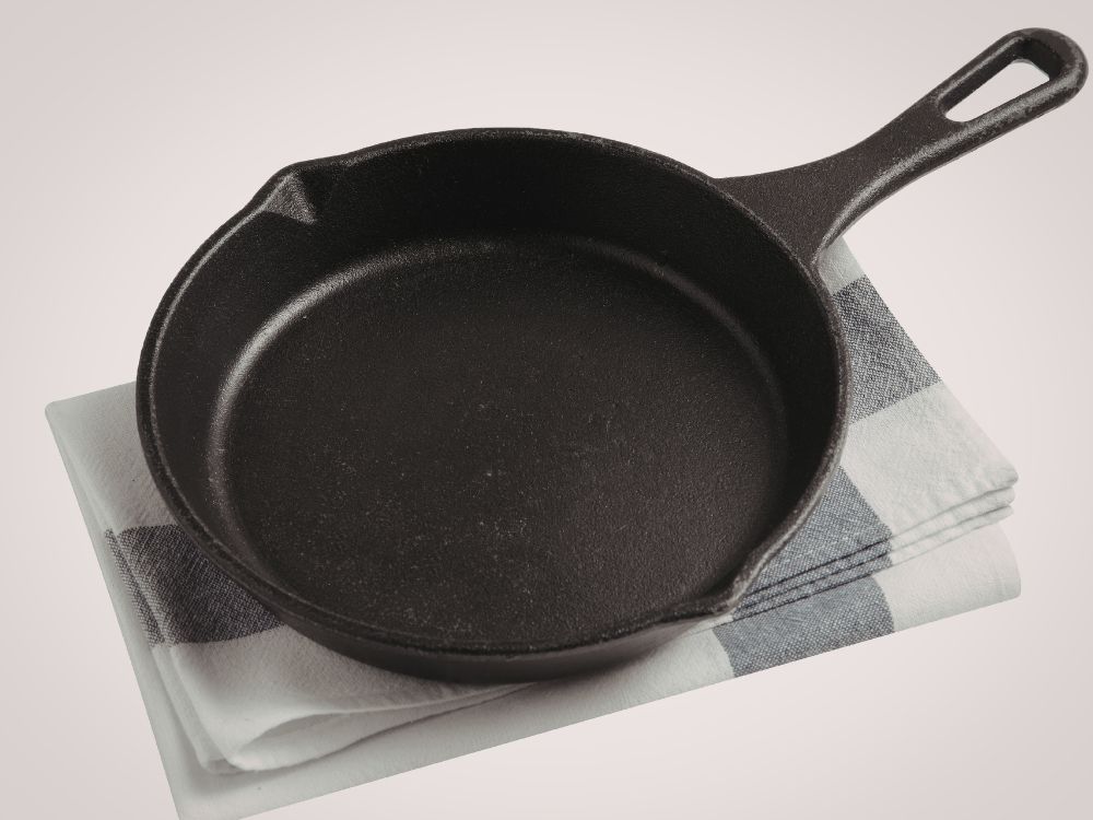 Panela de ferro fundido preta apoiada sobre pano de cozinha, destacando material resistente que exige cuidados para não enferrujar.