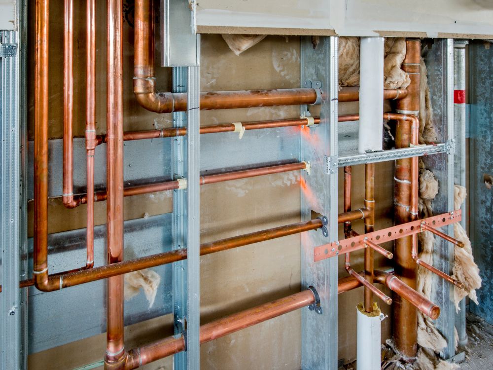 Tubulações de cobre e estrutura hidráulica instaladas em parede de construção civil, exemplificando o que é projeto hidrossanitário em uma obra residencial.