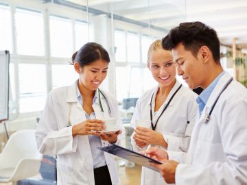 Profissionais da saúde em ambiente hospitalar conversando e analisando informações em prancheta, representando formação, estudo e trabalho em equipe na área da saúde.
